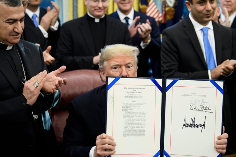 President Donald Trump shows H.R. 390, a bill that activates support for Christians and Yazidis targeted by ISIS, after signing it in the Oval Office on Tuesday.